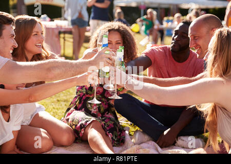 Group Of Friends Sitting On Rug At Summer Garden Fete And Making Toast Stock Photo