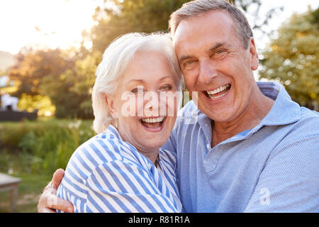 Portrait Of Loving Senior Couple Hugging Outdoors In Summer Park Against Flaring Sun Stock Photo