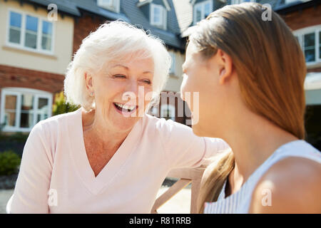 Granddaughter Sitting On Bench With Grandmother During Visit To Retirement Home Stock Photo