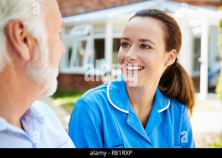 Senior Man Sitting On Bench And Talking With Nurse In Retirement Home Stock Photo