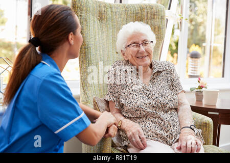 Senior Woman Sitting In Chair And Talking With Nurse In Retirement Home Stock Photo