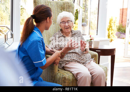 Senior Woman Sitting In Chair And Talking With Nurse In Retirement Home Stock Photo