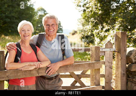 Portrait Of Senior Couple Hiking In Lake District UK Looking Over Wooden Gate Stock Photo