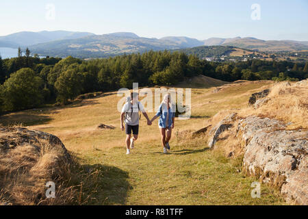 Couple Climbing Hill On Hike Through Countryside In Lake District UK Together Stock Photo