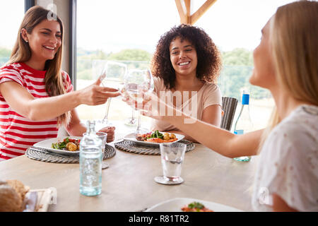 Multi ethnic group of three young adult women making a toast,celebrating with wine glasses during a dinner party Stock Photo