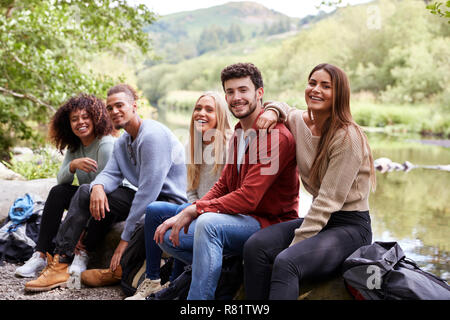 Multi ethnic group of five young adult friends taking a break sitting on rocks by a stream during a hike, portrait Stock Photo