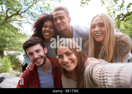 Multi ethnic group of five young adult friends pose to camera while taking a selfie during a break in a hike Stock Photo
