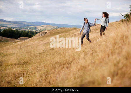 Mixed race young adult couple holding hands while walking walking down a hill during a mountain hike Stock Photo