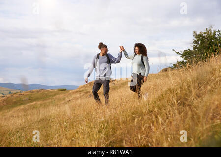 Young adult mixed race couple walking down a hill hand in hand during a mountain hike Stock Photo