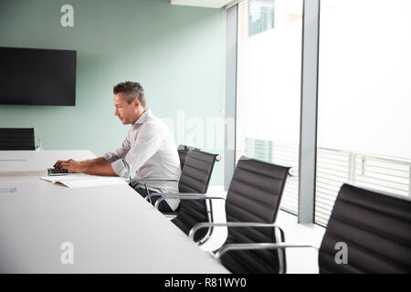 Casually Dressed Mature Businessman Working On Laptop At Boardroom Table In Meeting Room Stock Photo