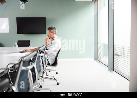 Casually Dressed Mature Businessman Working On Laptop At Boardroom Table In Meeting Room Stock Photo