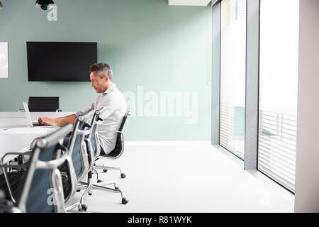 Casually Dressed Mature Businessman Working On Laptop At Boardroom Table In Meeting Room Stock Photo