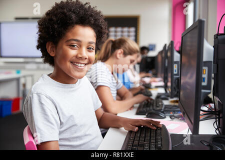 Portrait Of Smiling Male Pupil Sitting In Line Of High School Students Working at Screens In Computer Class Stock Photo