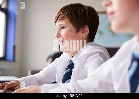 High School Students Wearing Uniform Sitting And Working Around Table In Lesson Stock Photo