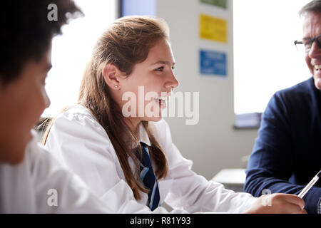 Male High School Tutor Sitting At Table With Students Teaching Lesson Stock Photo