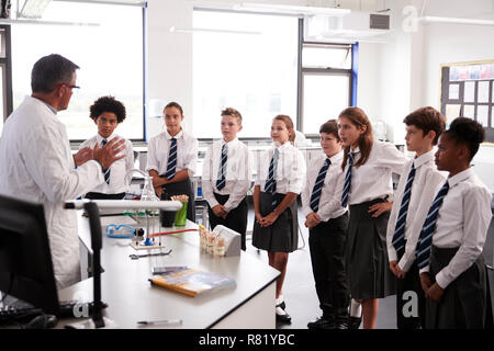 Male High School Tutor Teaching High School Students Wearing Uniforms In Science Class Stock Photo