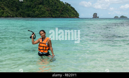 Woman standing in water in orange life jacket holding mask and snorkle Stock Photo