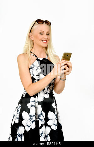 Attractive happy woman in pretty dress smiling whilst reading something on her mobile phone, taken against white background Stock Photo