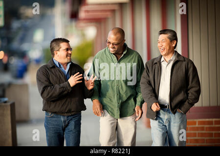 Three smiling middle aged men walking along a street. Stock Photo