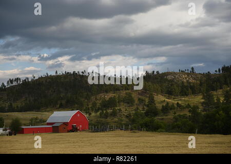 Farm in the countryside with red barn, tractor, hills and fields in the USA.