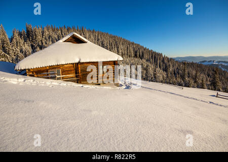 Human footprint path in white deep snow leading to small old wooden forsaken shepherd hut in mountain valley, spruce forest, woody dark hills, bright  Stock Photo
