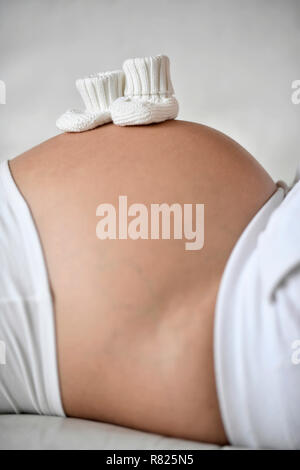 Woman in ninth month pregnant, baby shoes on belly, Germany Stock Photo