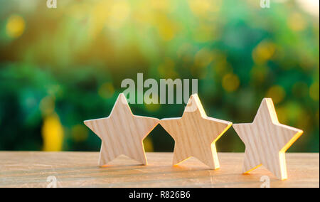 three wooden stars on a background of green bokeh background. The concept of the rating of hotels and restaurants, the evaluation of critics and visit Stock Photo