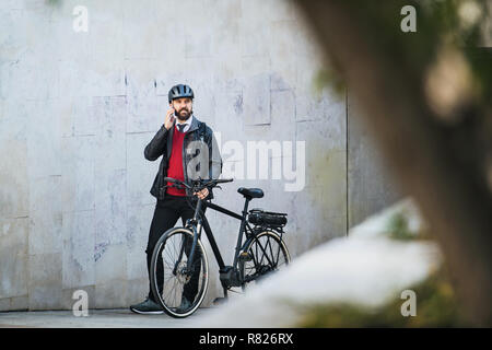 Businessman commuter with bicycle walking home from work in city, using smartphone. Stock Photo