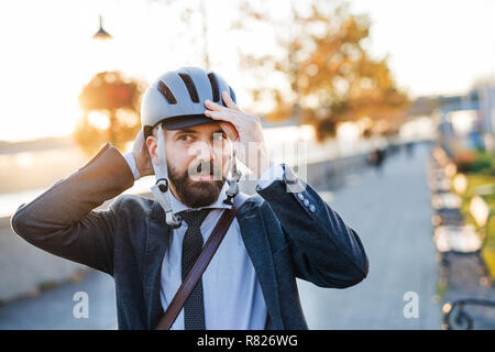 Businessman commuter traveling home from work in city, putting on a bicycle helmet. Stock Photo