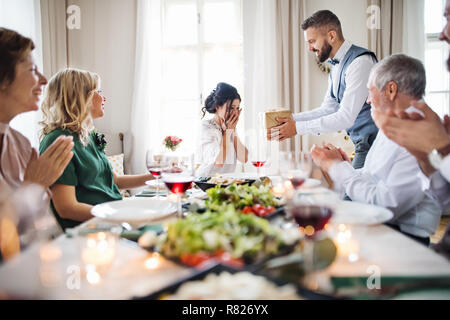 A man giving gift to a young surprised woman on a family birthday party. Stock Photo