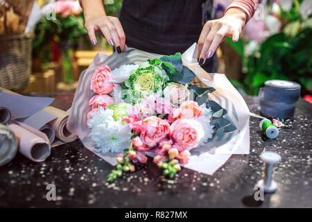 Picture of woman's hands touch bouqet paper. It is lying on table. Paper rolls and coil of thread are on table. Stock Photo