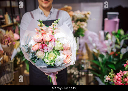 Cut view of young man in black apron holding bouquet of flowers. He stand in room full of different plants. Stock Photo