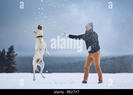 Friendship between pet owner and his dog. Young man playing with labrador retriever in winter landscape. Stock Photo