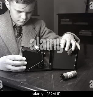 1950s, historical, an English schoolboy unloading the rear of a Kodak 'Brownie' box camera to put a a new film roll in. The Brownie was a popular film camera of the era being affordable and simple to use for those beginning the hobby of photography. Stock Photo