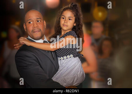 Father with a young daughter in his armsFather is wearing a black suit with a black tie and child has on a formal long neutral color dress. Stock Photo