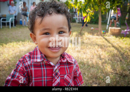 Happy one-year-old boy looking at the camera with a smile.  Closeup of toddler boy walking to camera at a family party in the backyard. Stock Photo