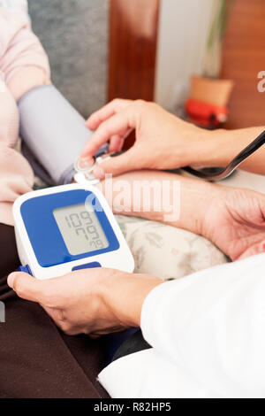 closeup of a caucasian doctor man, in a white coat, measuring the blood pressure of a senior caucasian patient woman with a sphygmomanometer, at her h Stock Photo