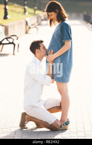 https://l450v.alamy.com/450v/r82hx2/young-man-kissing-the-belly-of-his-pregnant-wife-while-standing-on-one-knee-a-modern-couple-enjoying-a-healthy-walk-together-in-the-park-on-a-sunny-d-r82hx2.jpg