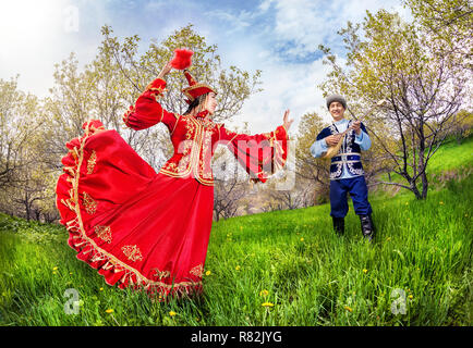Kazakh woman dancing in red dress and man playing dombra at Spring Blooming garden in Almaty, Kazakhstan, Central Asia Stock Photo