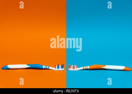 Worn / Used and New Toothbrush on a split  orange and blue background Stock Photo