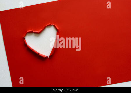 Ripped paper hole heart shaped on red paper background. Valentine's day celebration concept Stock Photo