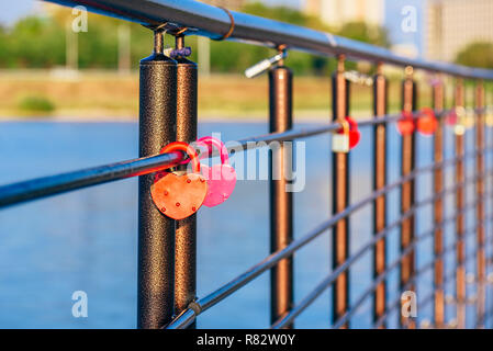 Colorful metal locks hanging on black railings in the sunrise light. Stock Photo