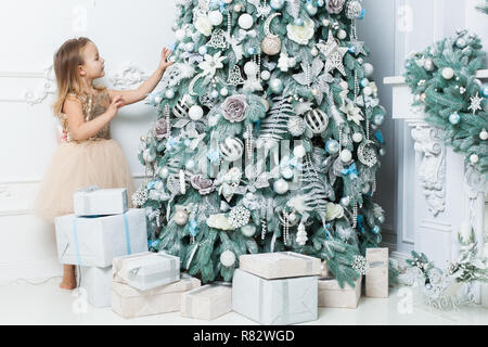 Little girl in a beautiful dress hangs decorations on the Christmas tree. Stock Photo