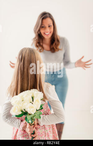 Cute daughter giving her mother Bouquet white roses for Mother's Day. Selective focus. Focus on foreground, on little girl and flowers. Stock Photo