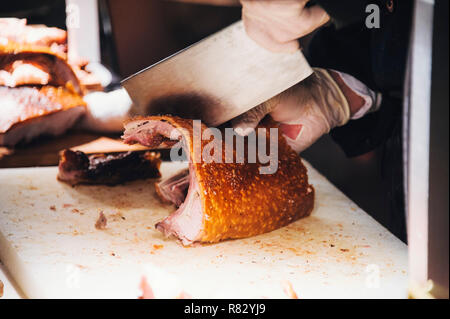 Close up view of hands chopping roast pig ribs with a large meat cleaver Stock Photo