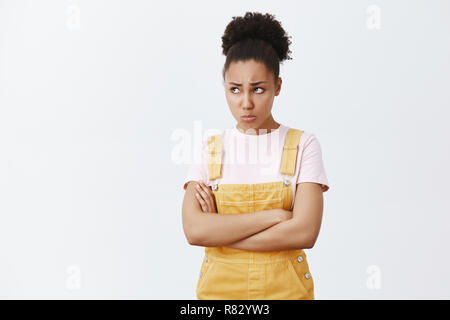 Offended upset and jealous young female student with dark skin, frowning and sulking, pursing lips, staring up while feeling insulted, holding hands crossed on chest from anger and disappointment Stock Photo