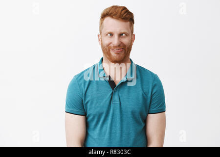 Waist-up shot of funny emotive and playful immature european male with ginger hair, squinting and rolling eyes aside, sticking out tongue, fooling around and aping, showing hilarious faces Stock Photo