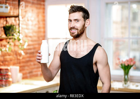 Portrait of a handsome sports man in black t-shirt drinking milk shake on the kitchen at home Stock Photo
