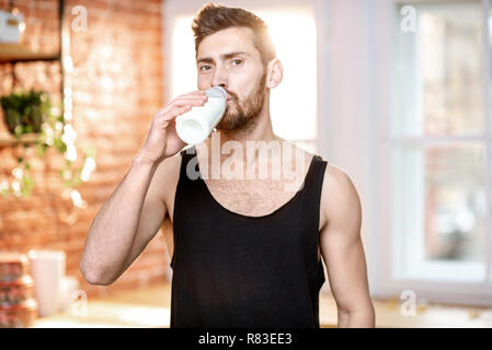 Handsome sports man in black t-shirt drinking milk shake standing on the kitchen at home Stock Photo