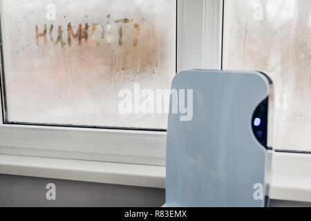 Dehumidifier with touch panel works by wet window in flat. Humidity written on window. High dampness concept. Stock Photo